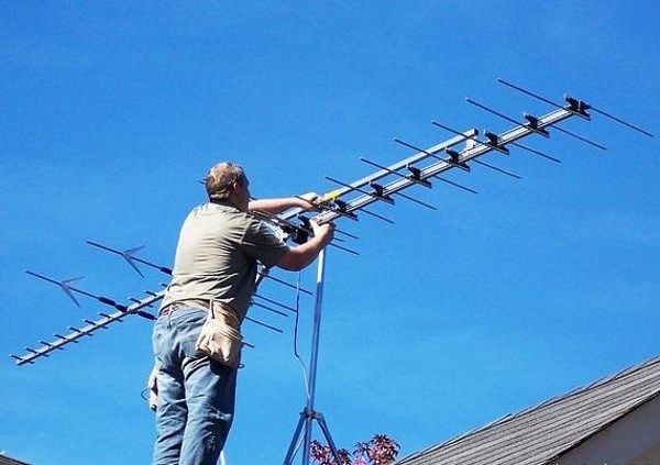 мастер устанавливает антенну на крыше частного дома